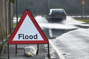 motorist driving through flood waters with warning sign in foreground
