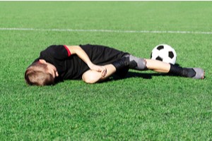Young soccer player lying on field holding his injured knee
