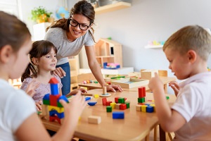 teacher with children playing with colorful wooden didactic toys at kindergarten