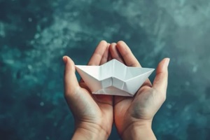 paper boat is held in the hands against an isolated toned background