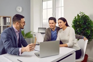 portrait of happy caucasian couple sitting with a business broker or insurance agent showing project on a laptop screen