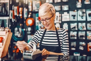 female worker with short blonde hair and eyeglasses using cash register while standing in bicycle store